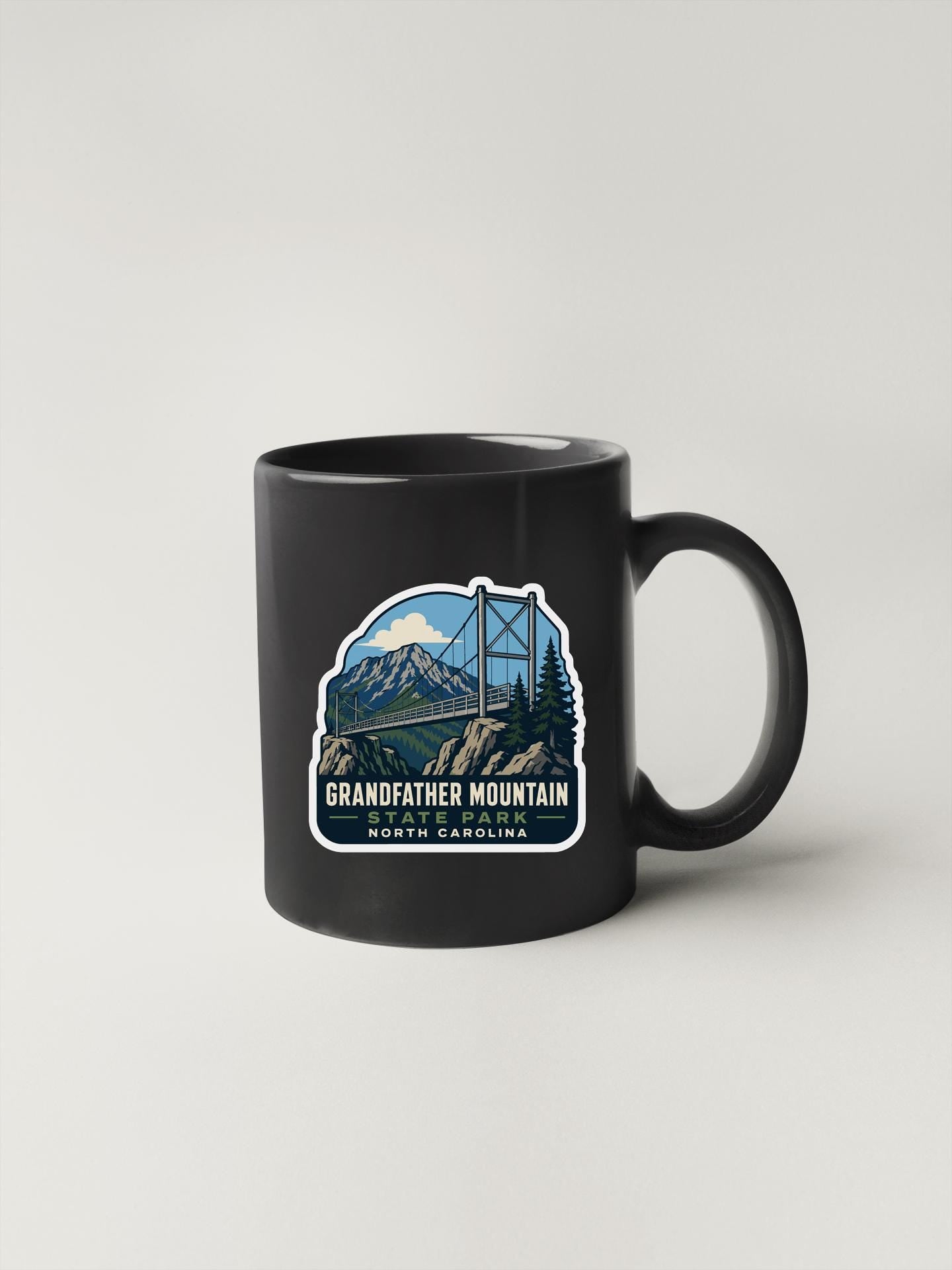 A black coffee mug with a graphic design depicting a mountain landscape and a bridge.