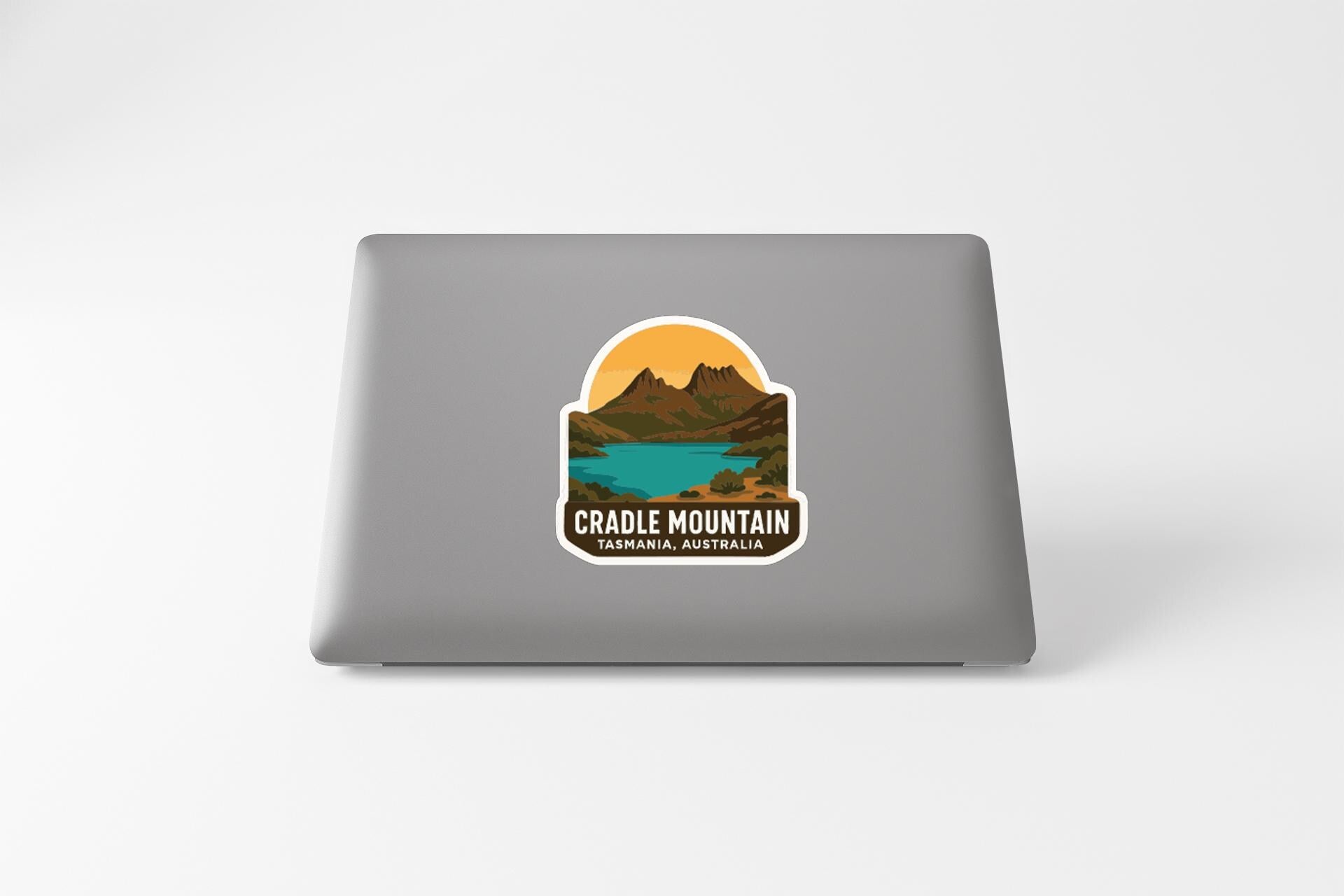 a sticker with a mountain landscape and a lake, with the text "Cradle Mountain" and "Tasmanian Australia" printed on it.