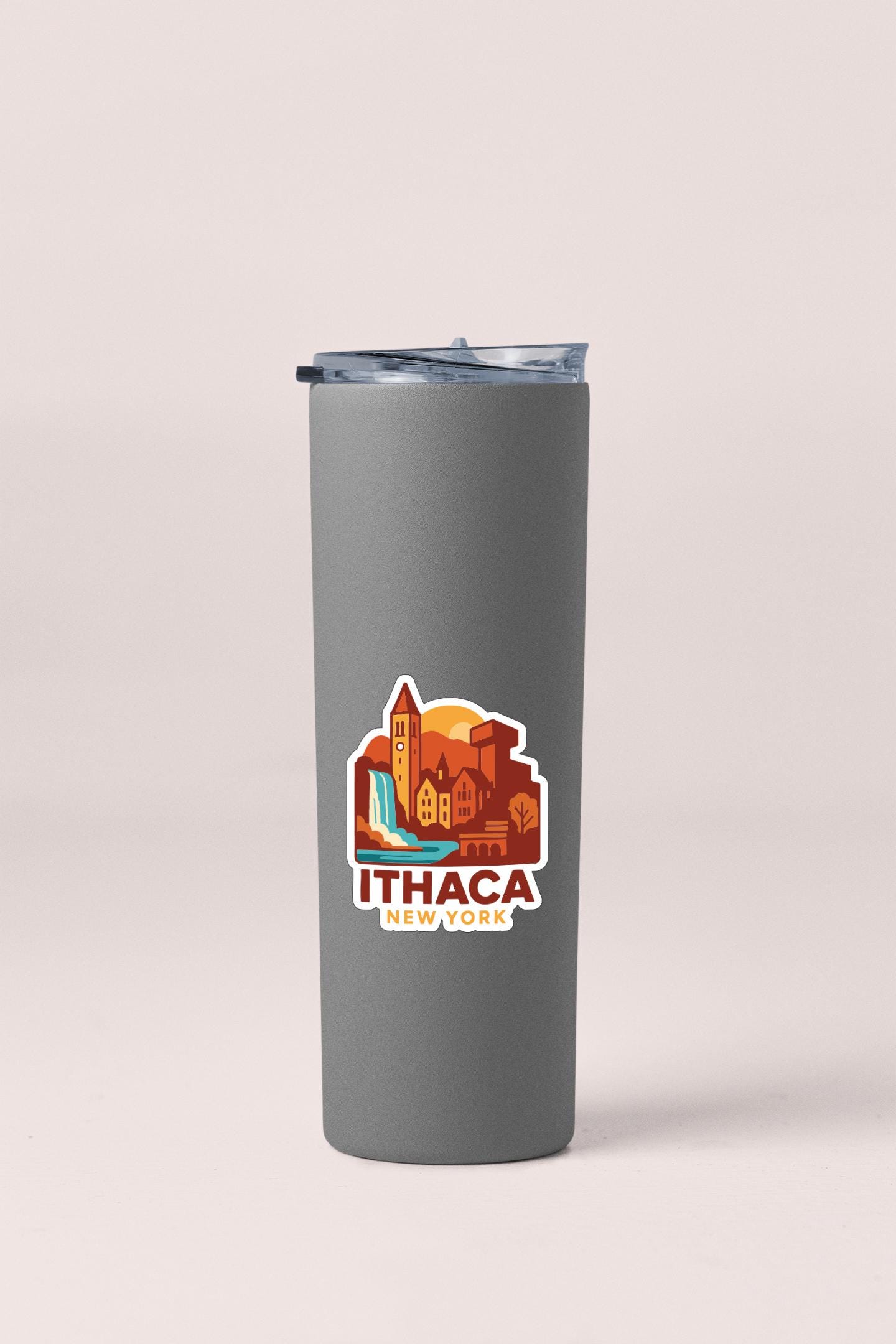 A gray insulated tumbler with a lid and a sticker depicting a cityscape with a waterfall.