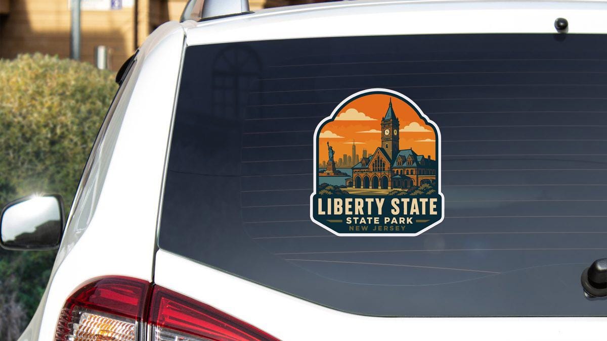 A sticker on the rear window of a white car, depicting a city skyline with a clock tower, indicating Liberty State State Park in New Jersey.