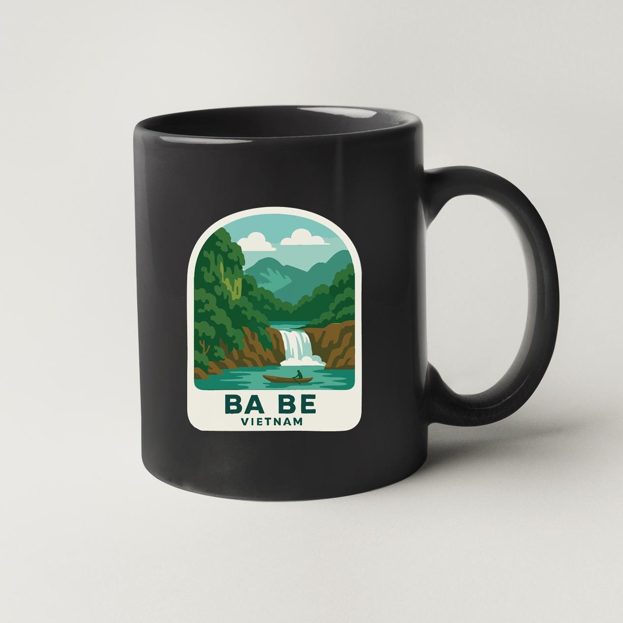 A black coffee mug with a graphic design depicting a waterfall and a boat in a river, along with the text "BA BE VETNAM".