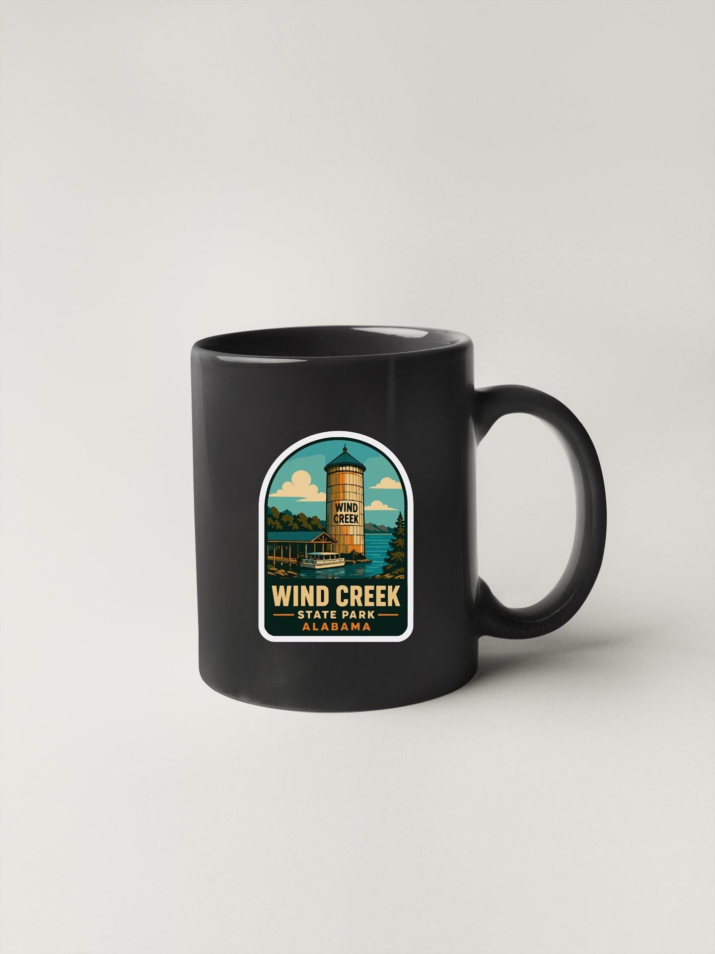 A black coffee mug with a graphic design depicting a tower and a lake, along with the text "Wind Creek State Park, Alabama".