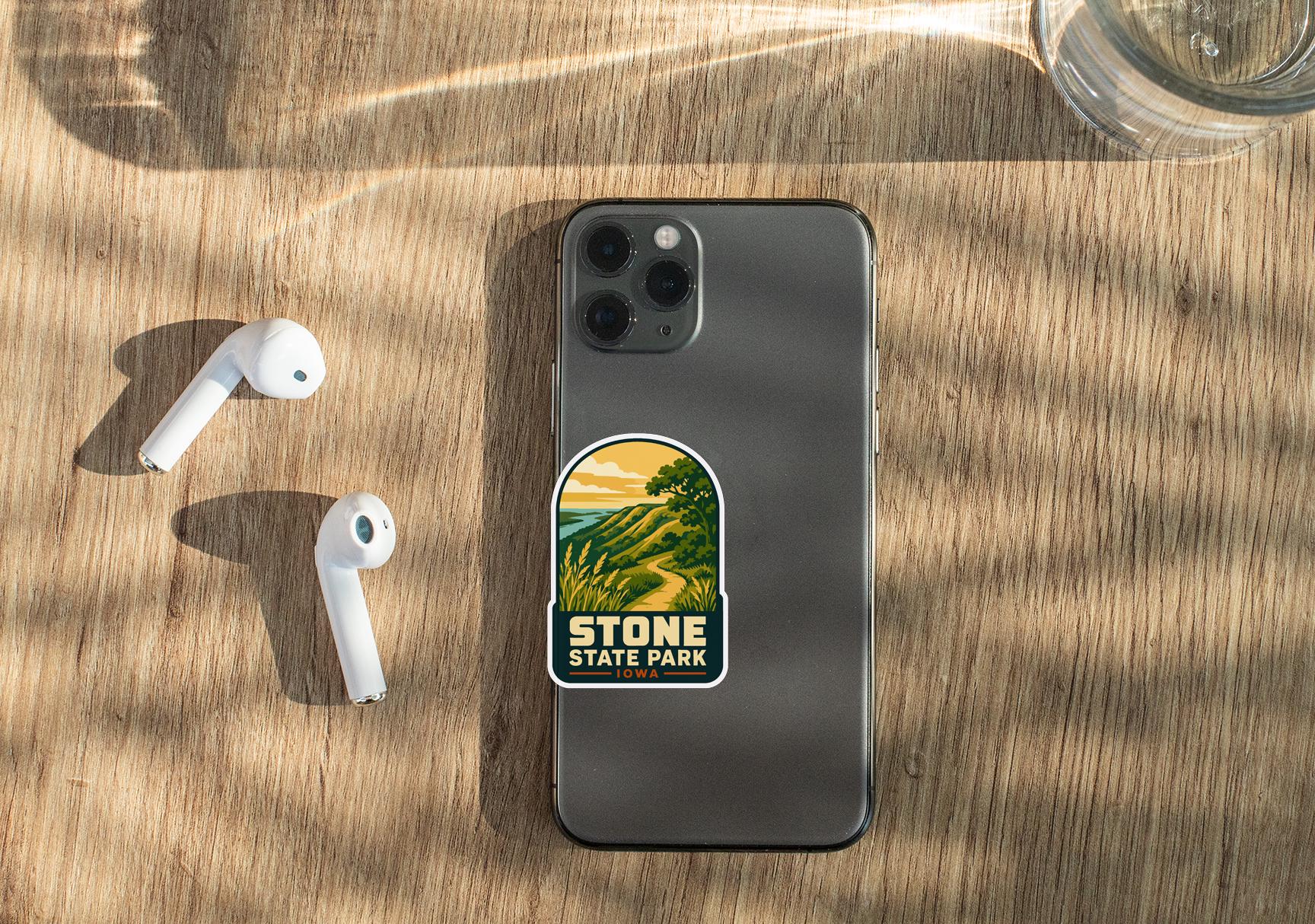 a smartphone with a sticker on the back, placed on a wooden surface alongside a pair of white earbuds and a glass of water.