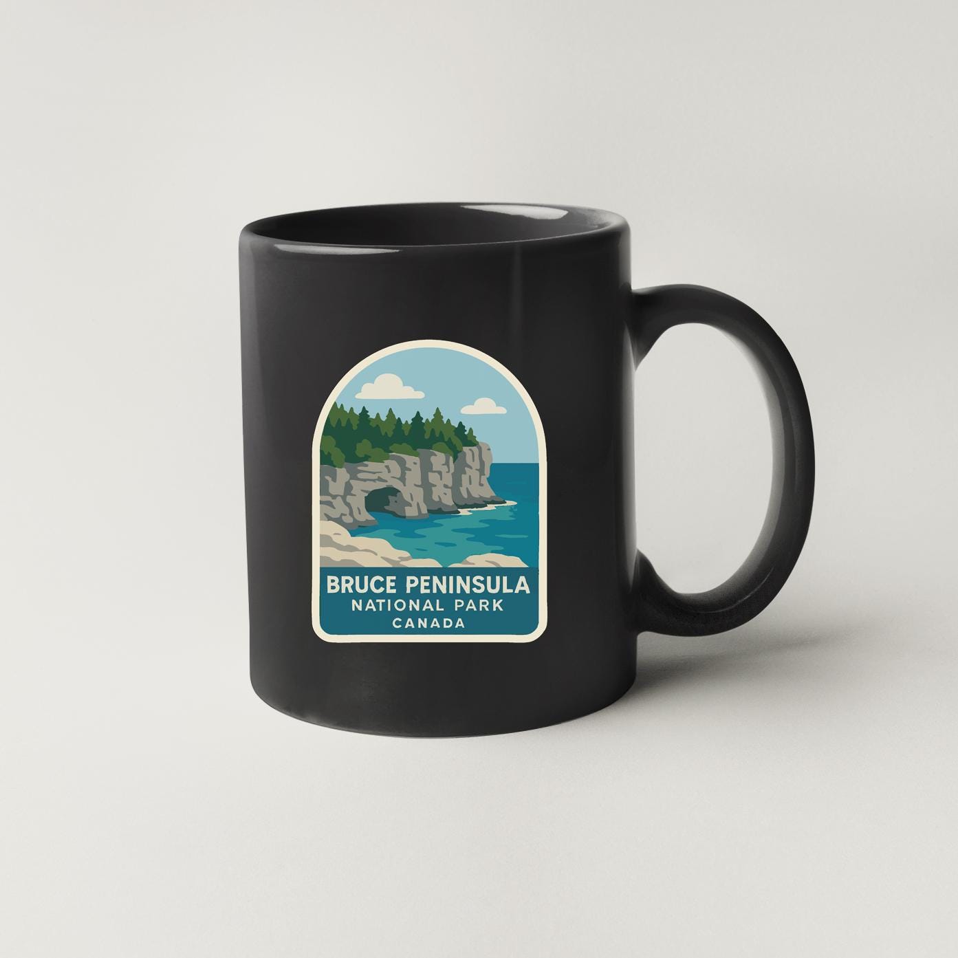 A black coffee mug with a label that features a scenic image of the Bruce Peninsula National Park in Canada.