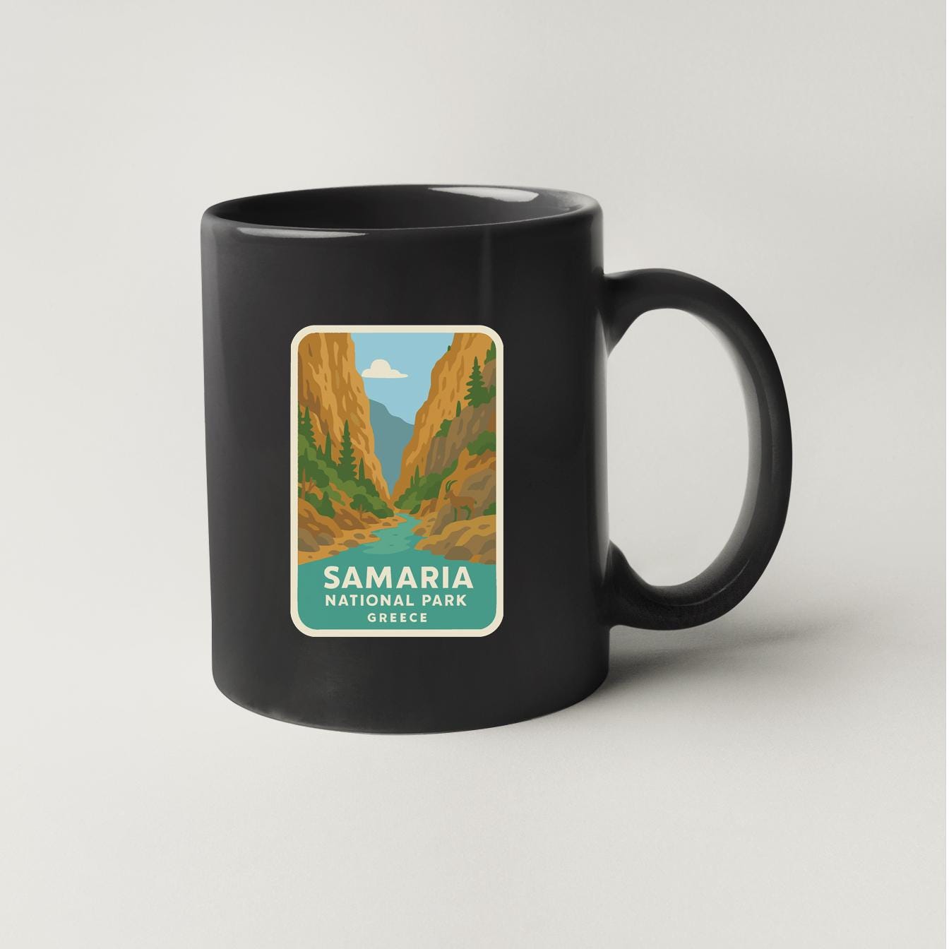 A black coffee mug with a sticker depicting a scenic landscape of Samaria National Park in Greece.