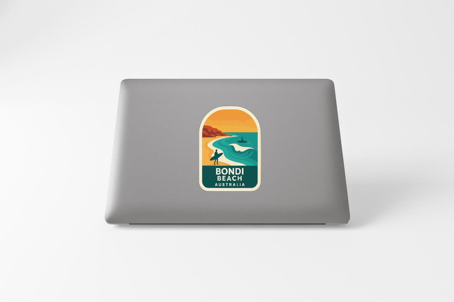 A sticker on the back of a laptop, depicting a beach scene with a surfer and a sunset.