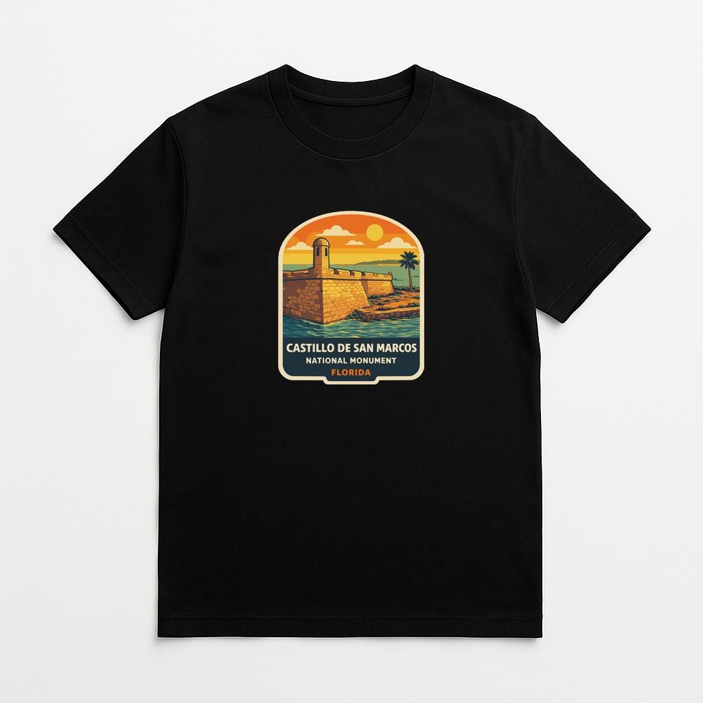 A black t-shirt with a graphic design depicting a lighthouse and a beach scene, along with the text "CASTILLO DE SAN MARCOS NATIONAL BONUS".