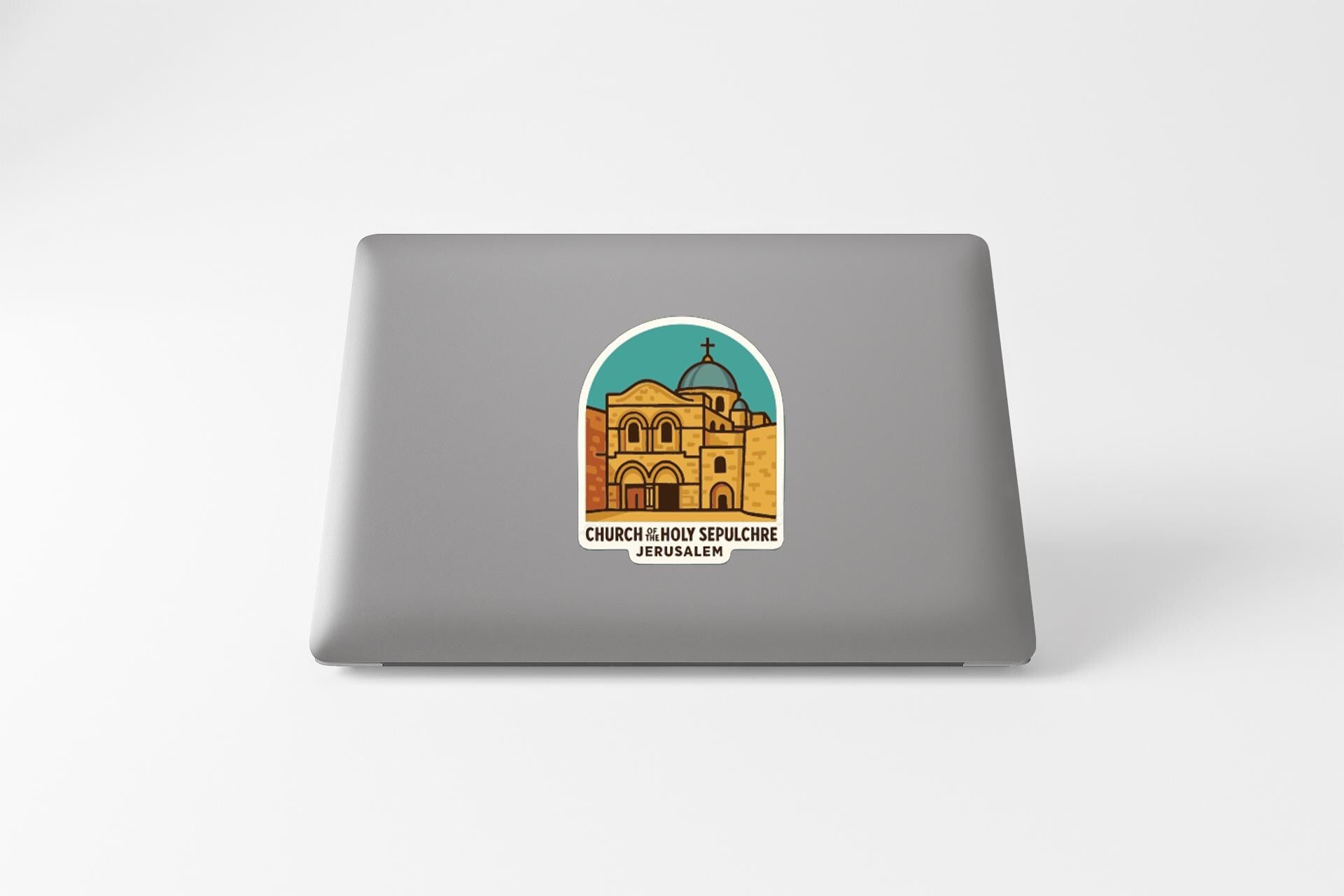 a sticker on the back of a laptop, depicting a building with a dome and arches, and the text "CHURCH IN BOSTON SPELUNG JERUSALEM" below the illustration.