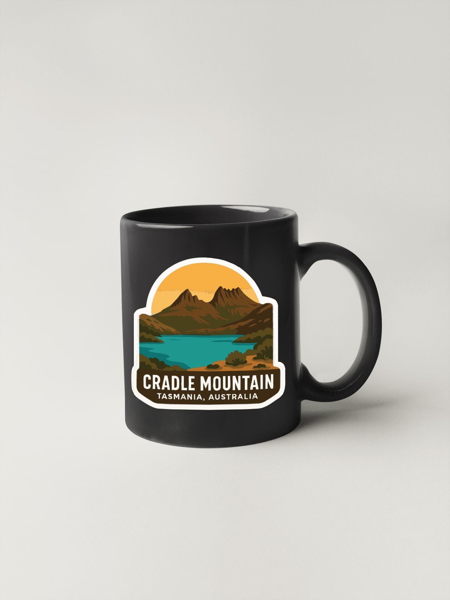 A black coffee mug with a graphic design depicting Cradle Mountain, a famous landmark in Tasmania, Australia.