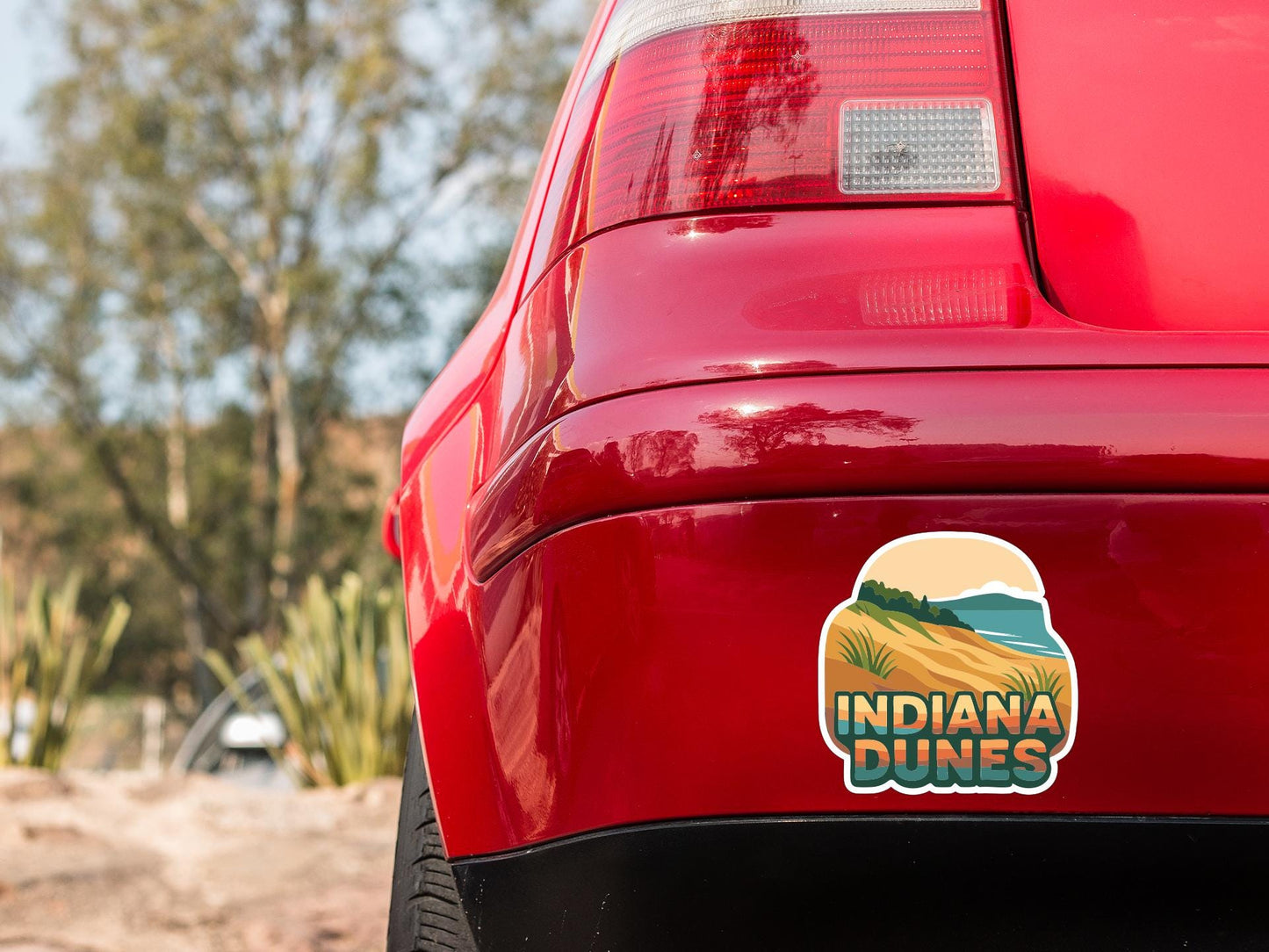 the rear end of a red car with a sticker on the trunk that says "Indiana Dunes".