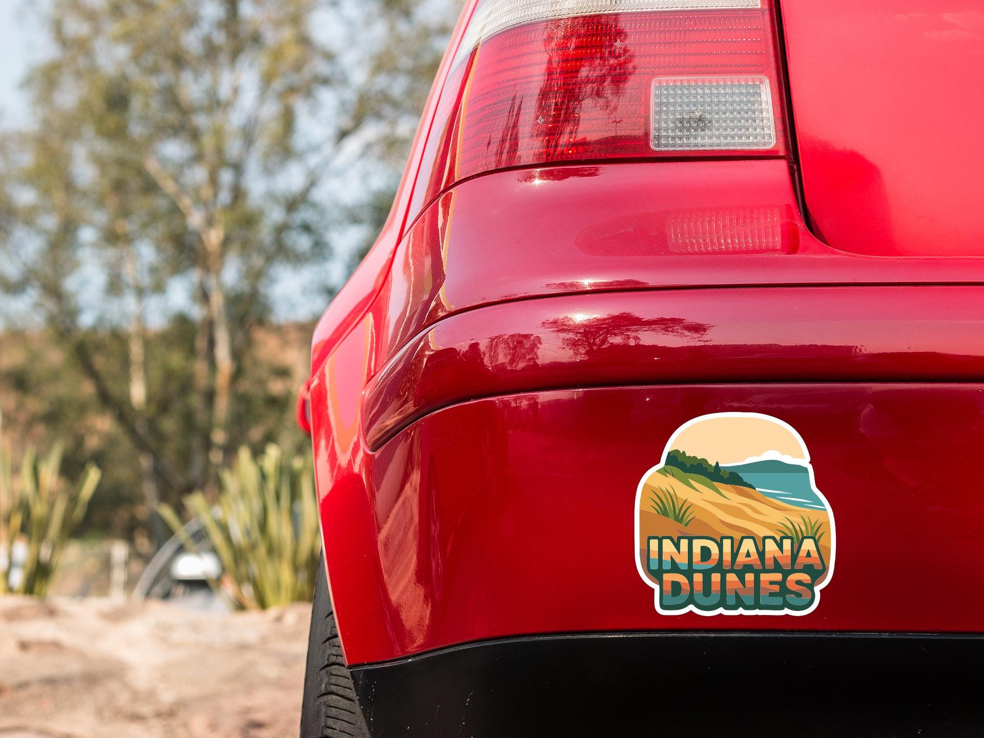 the rear end of a red car with a sticker on the trunk that says "Indiana Dunes".