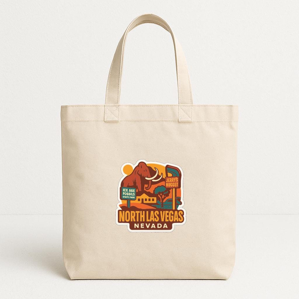 A beige tote bag with a printed graphic of a desert landscape and a sign that says "NORTH LAS VEGAS NEVADA".