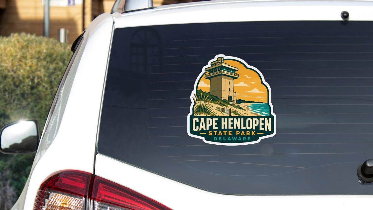 A sticker on the rear window of a white vehicle, depicting a lighthouse and the text "Cape Henlopen State Park, Delaware".