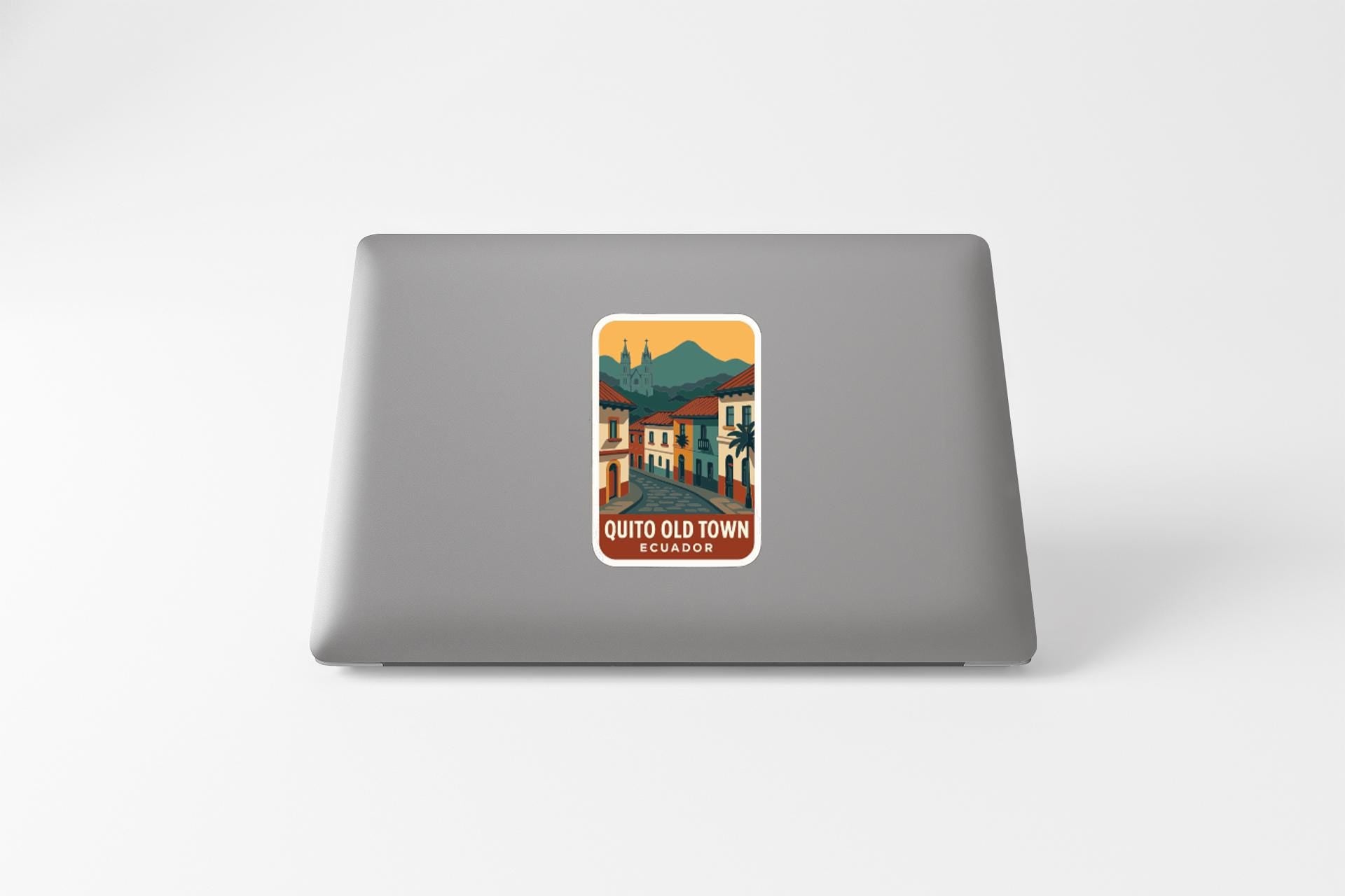 A sticker on the back of a laptop, depicting a colorful illustration of a town or village with buildings, roads, and mountains in the background.