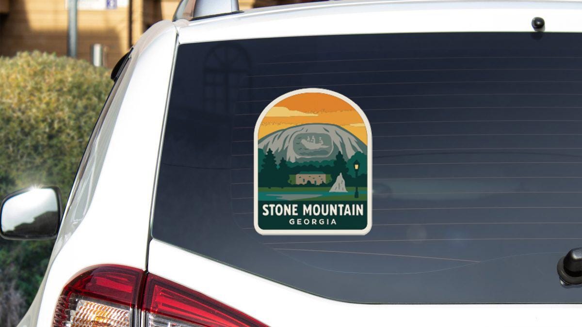 a sticker on the rear window of a car, depicting a scenic mountain landscape with a cabin and a lake.