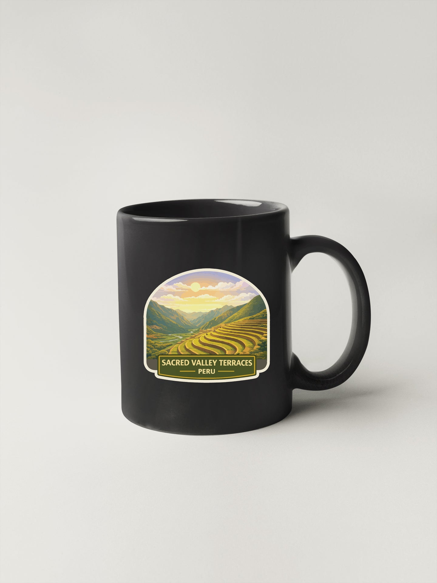 A black coffee mug with a graphic design depicting a scenic landscape with mountains, fields, and a sunset.