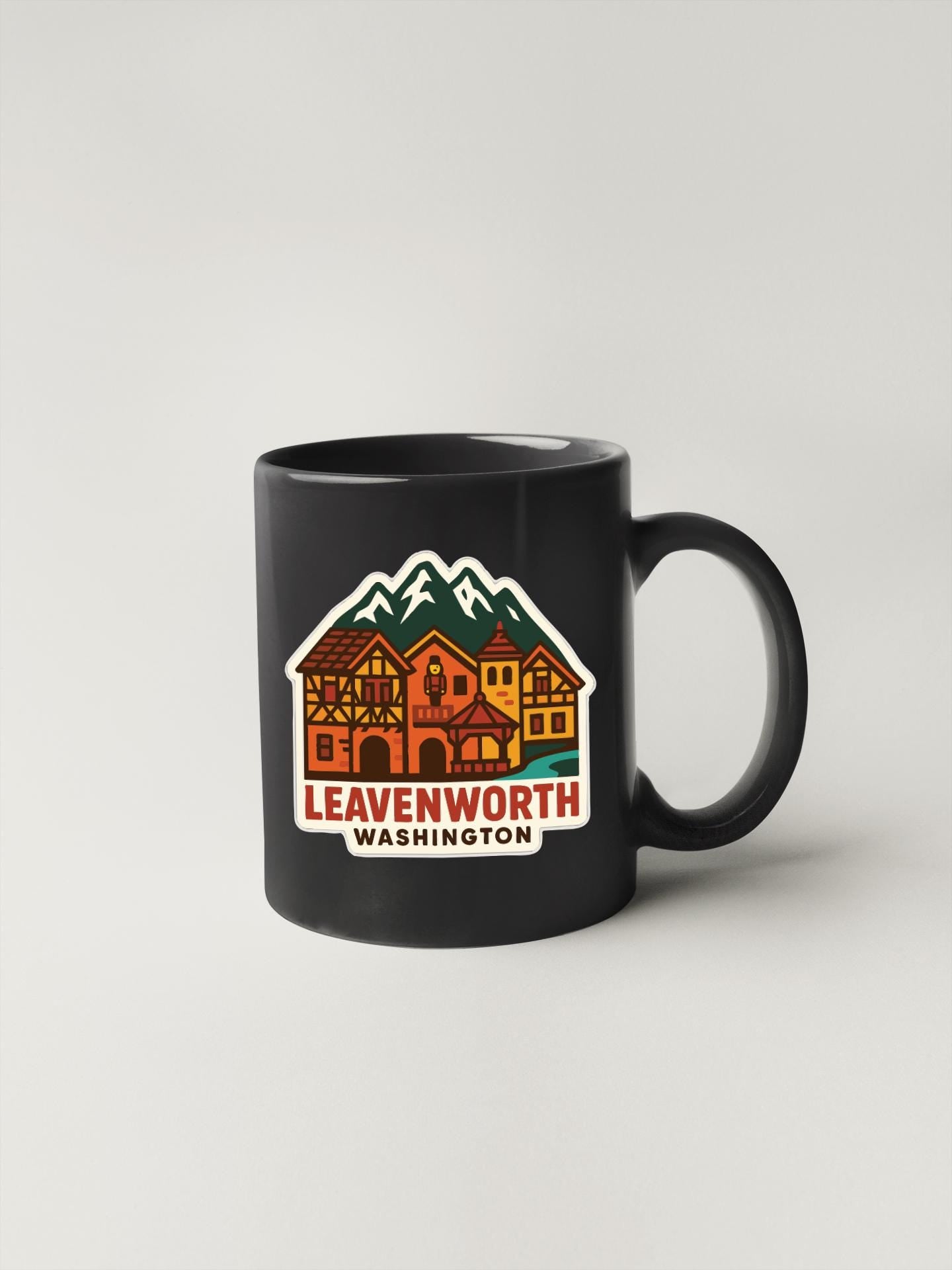 A black coffee mug with a colorful illustration of a village and mountains on it, along with the text "LEAENWORTH WASHINGTON".