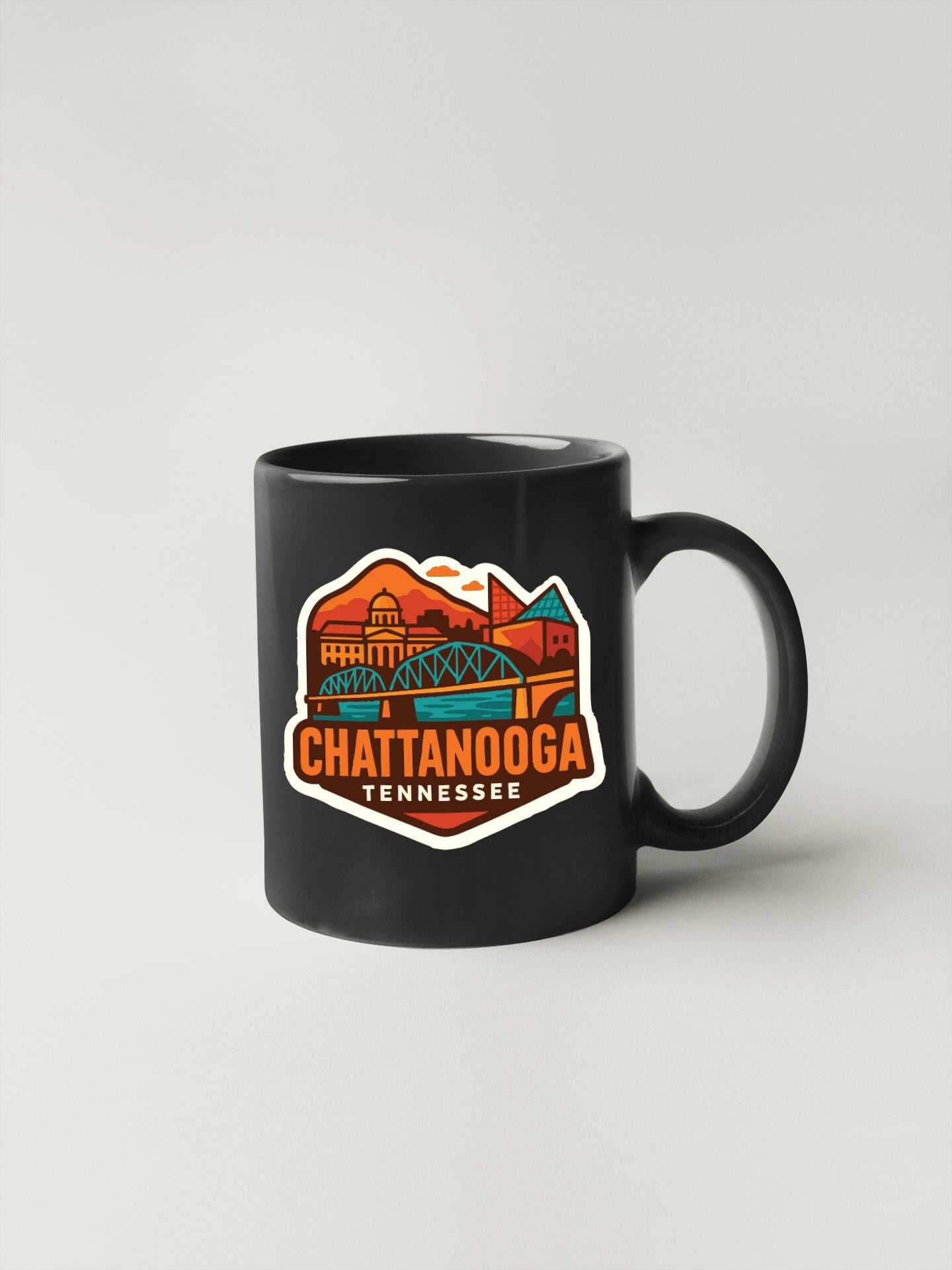A black coffee mug with a colorful graphic depicting a scenic view of Chattanooga, Tennessee.