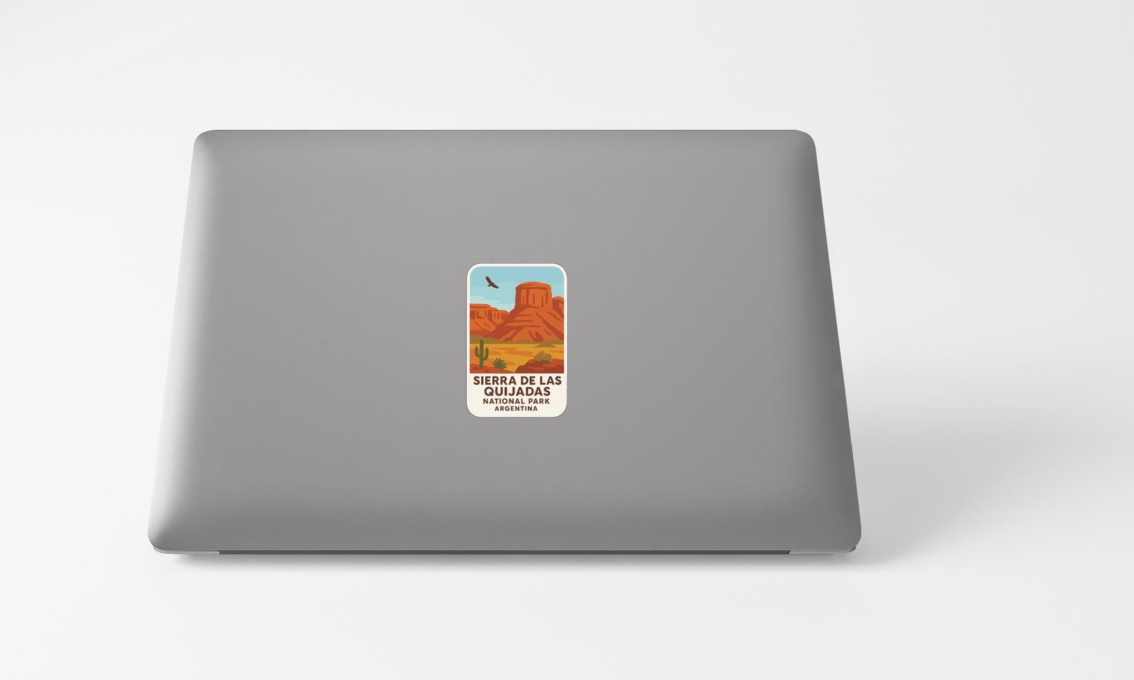A sticker on the back of a laptop, depicting a desert landscape with mountains and a bird in flight.