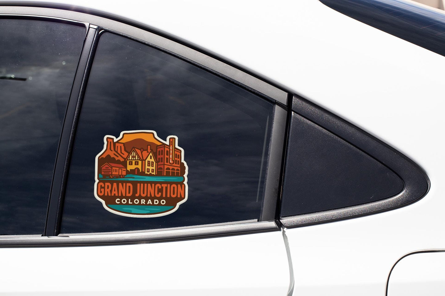 A car window with a sticker on it, featuring a colorful illustration of a town or city with mountains in the background.