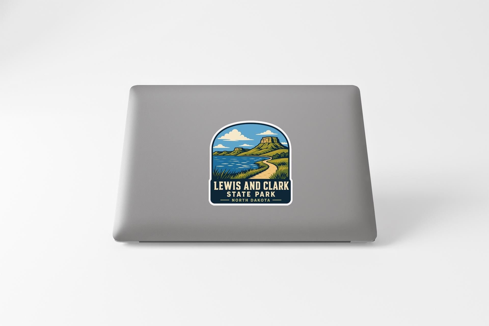 A sticker on the back of a laptop, depicting a scenic landscape with mountains, a river, and a sky with clouds.