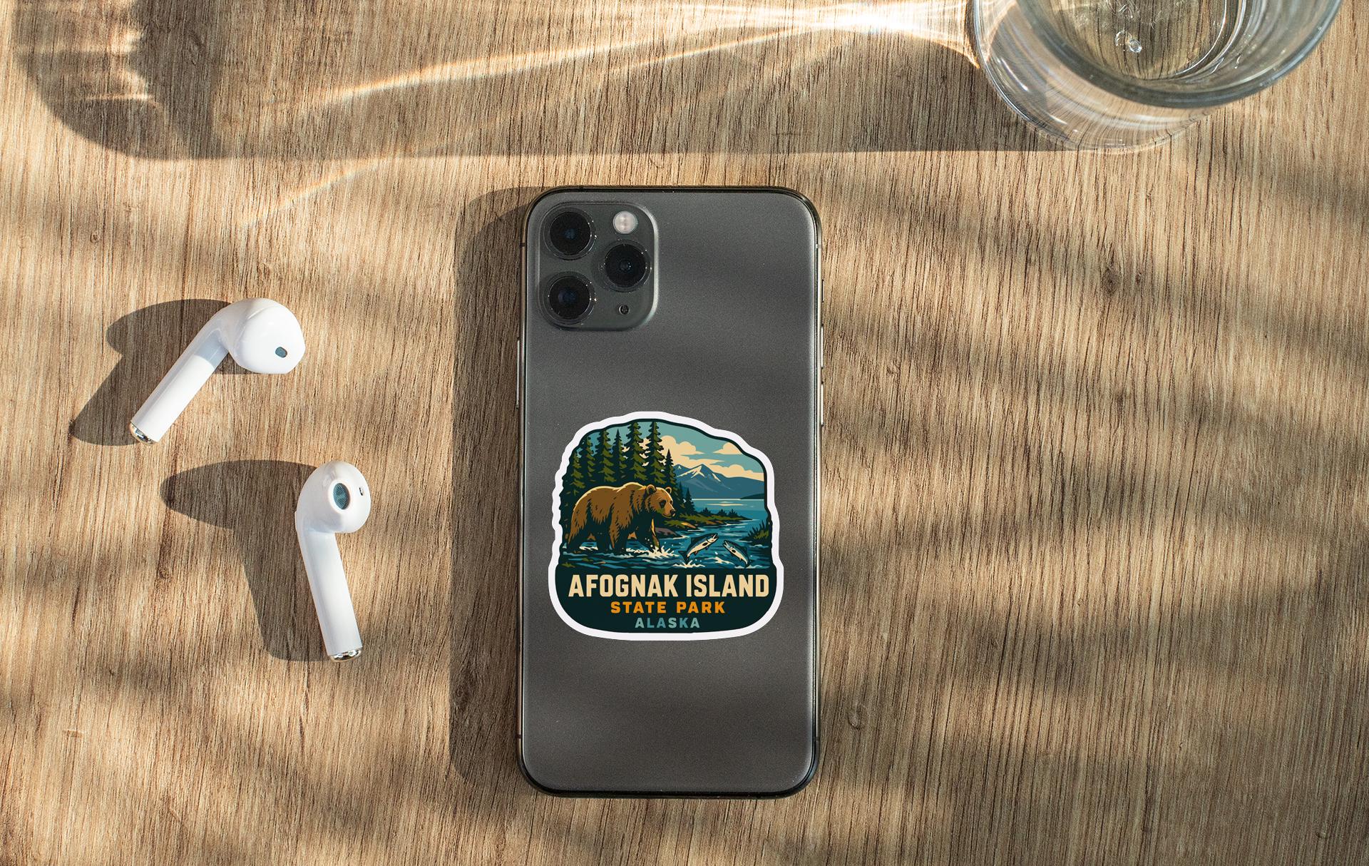 a smartphone with a sticker on it, placed on a wooden surface alongside a pair of white earbuds and a glass of water.
