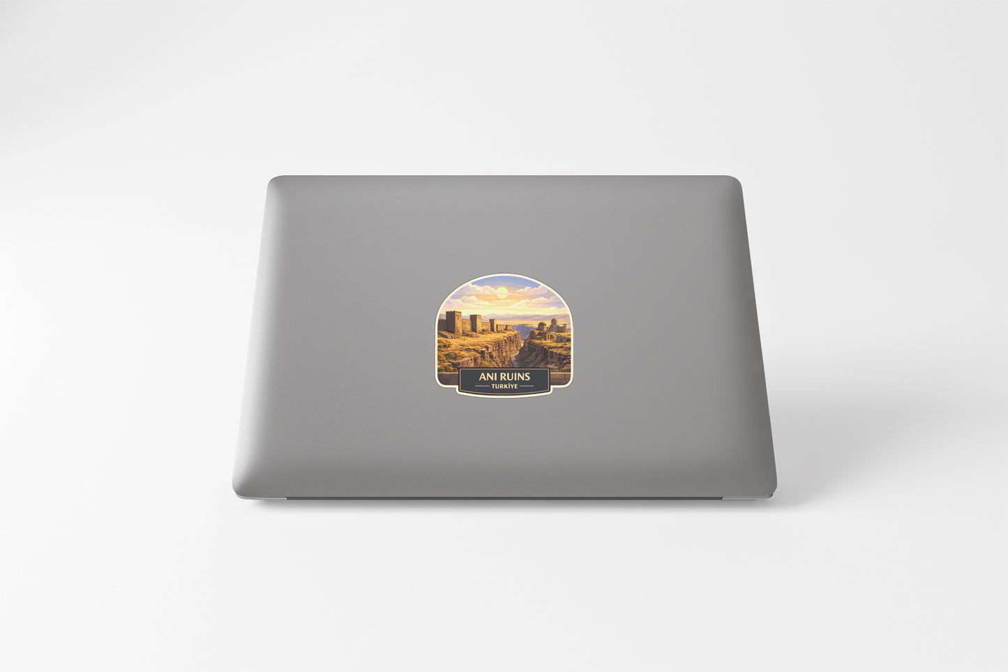 a sticker on the back of a laptop that depicts a scenic landscape with mountains and a city in the background.