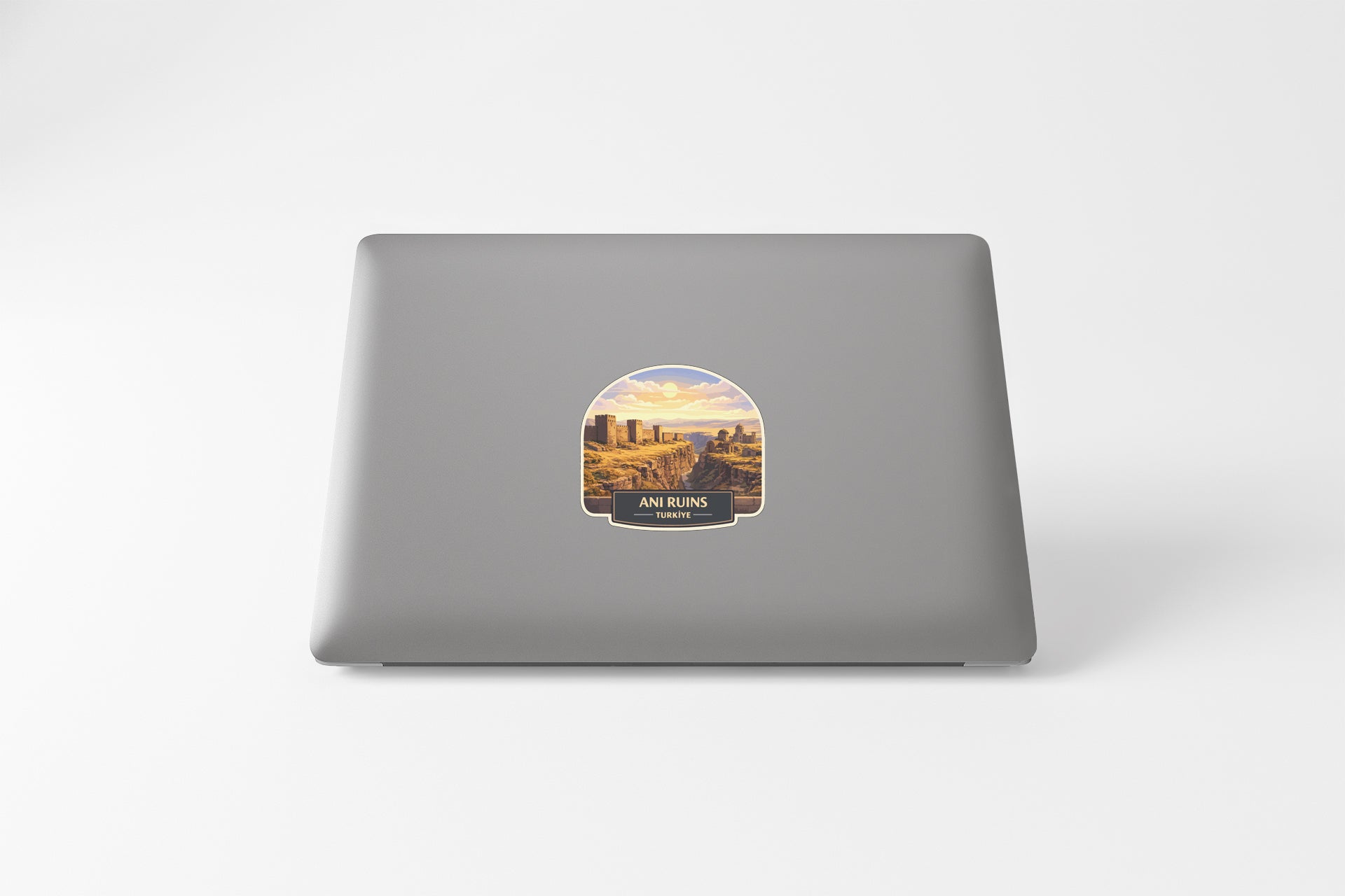 a sticker on the back of a laptop that depicts a scenic landscape with mountains and a city in the background.