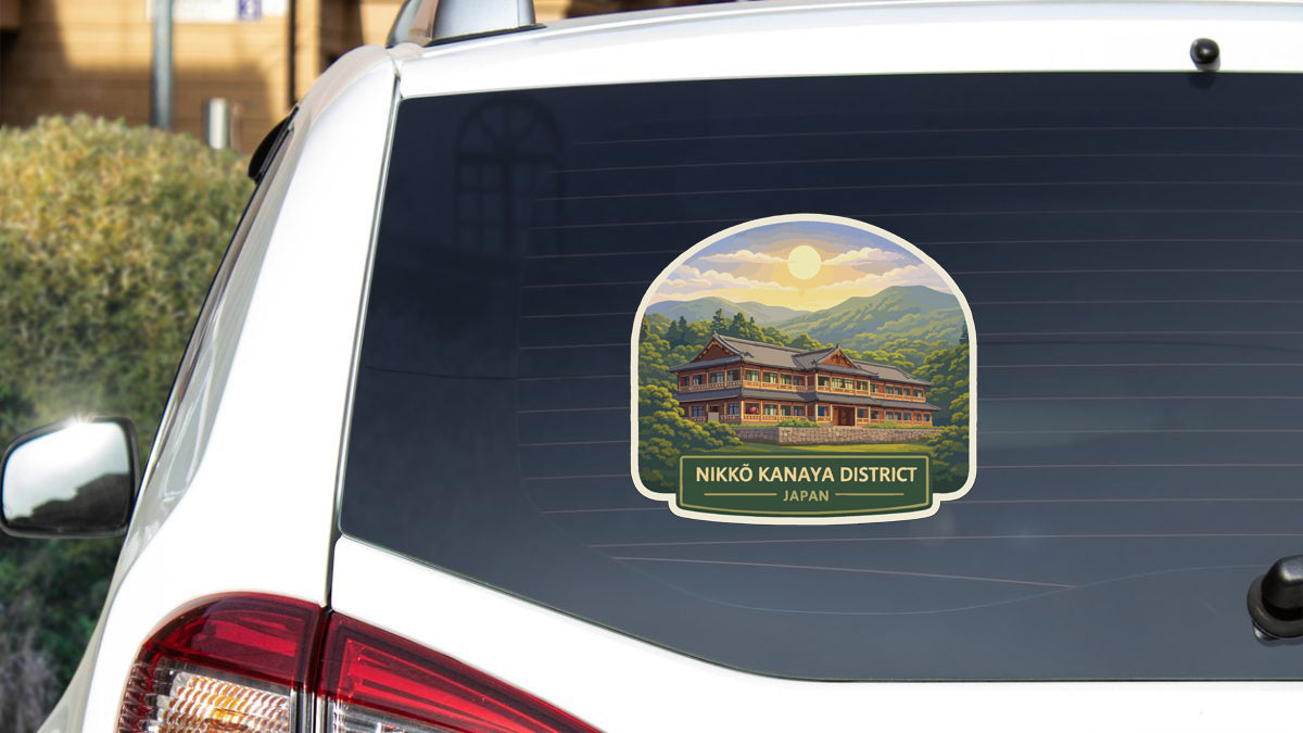 A sticker on the rear window of a white car, depicting a traditional Japanese house surrounded by mountains and trees.