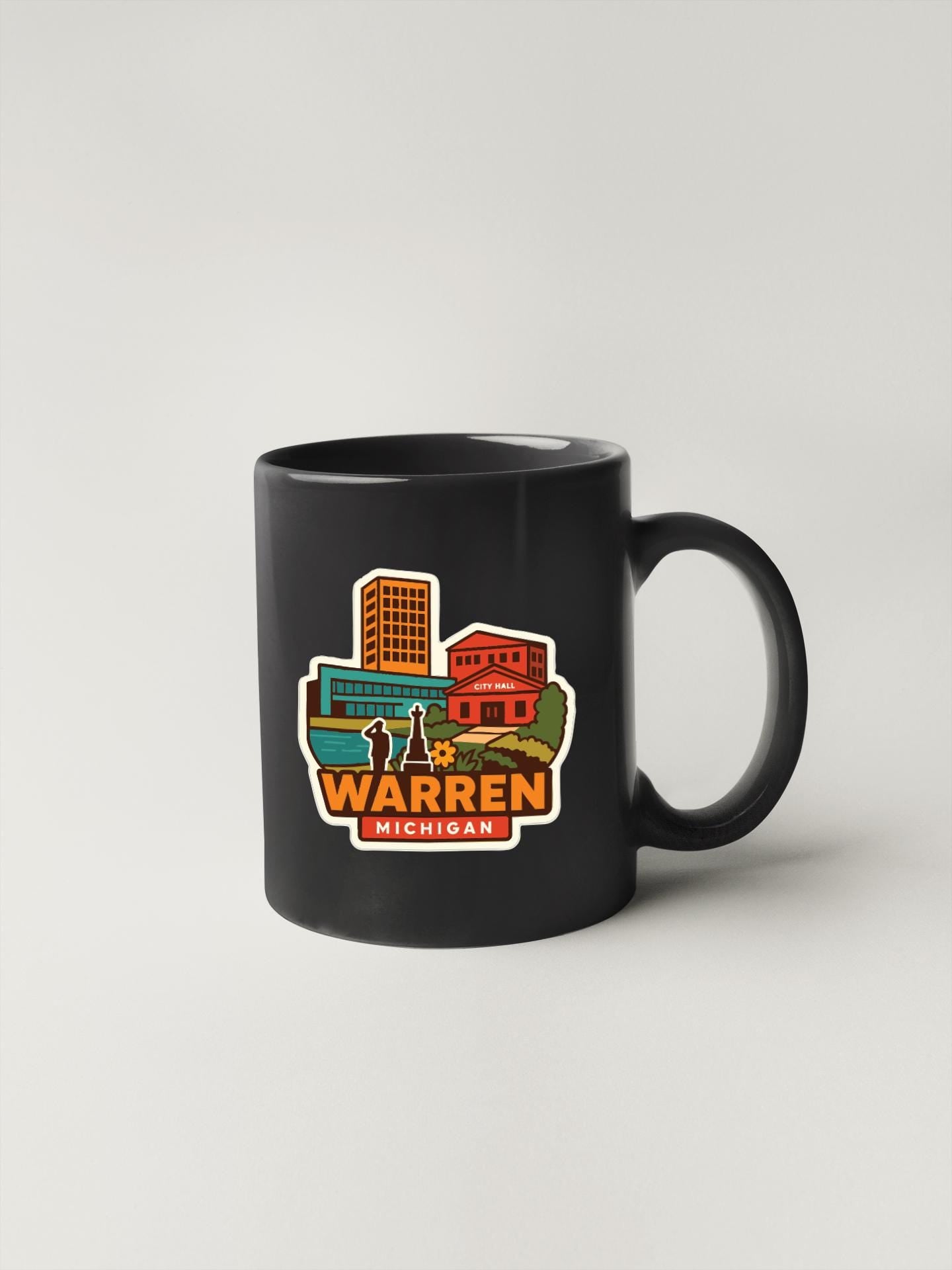 A black coffee mug with a colorful sticker depicting a cityscape and the text "WARREN MICHIGAN".