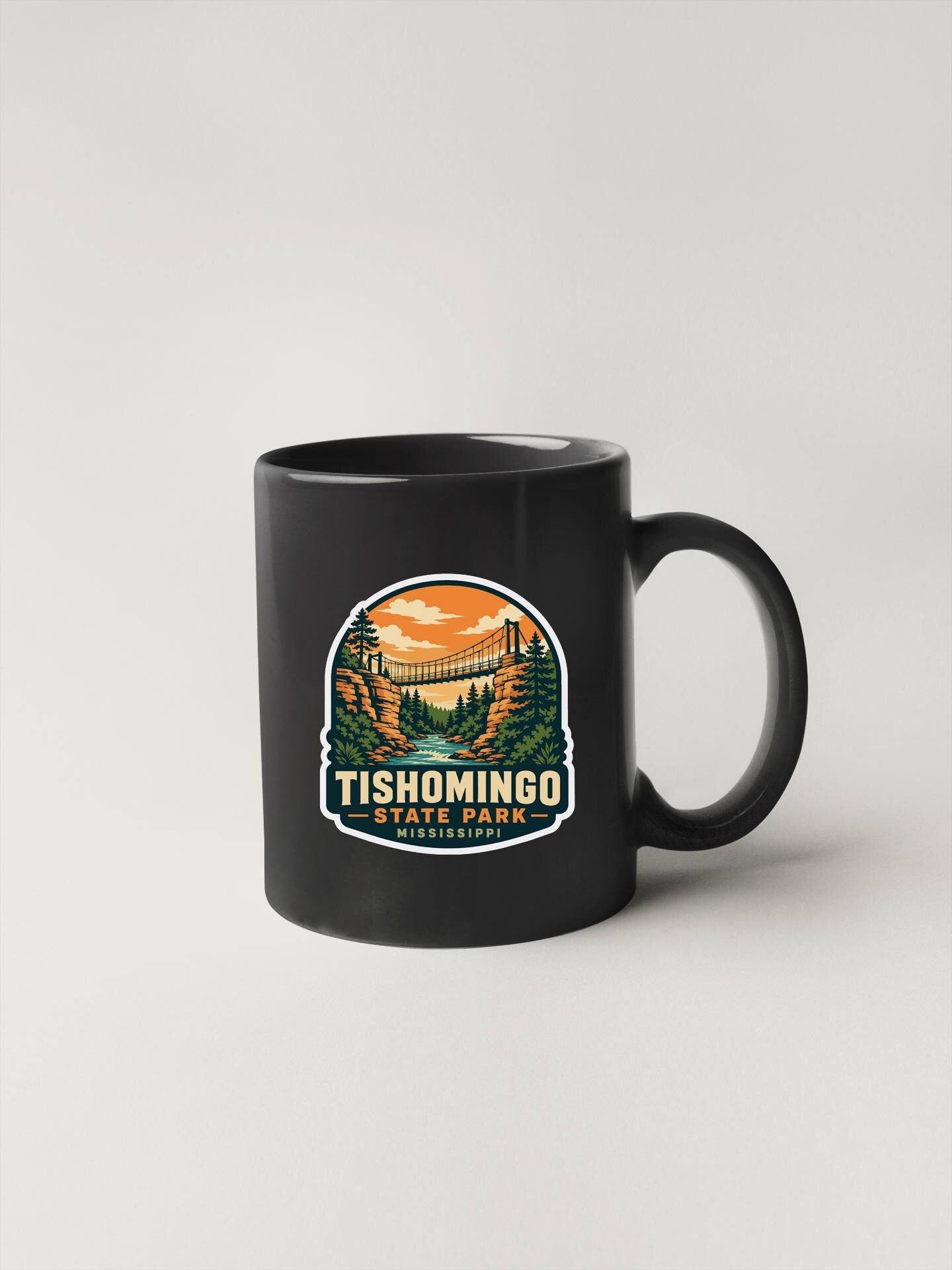 A black coffee mug with a graphic design depicting a scenic landscape with a bridge and trees.