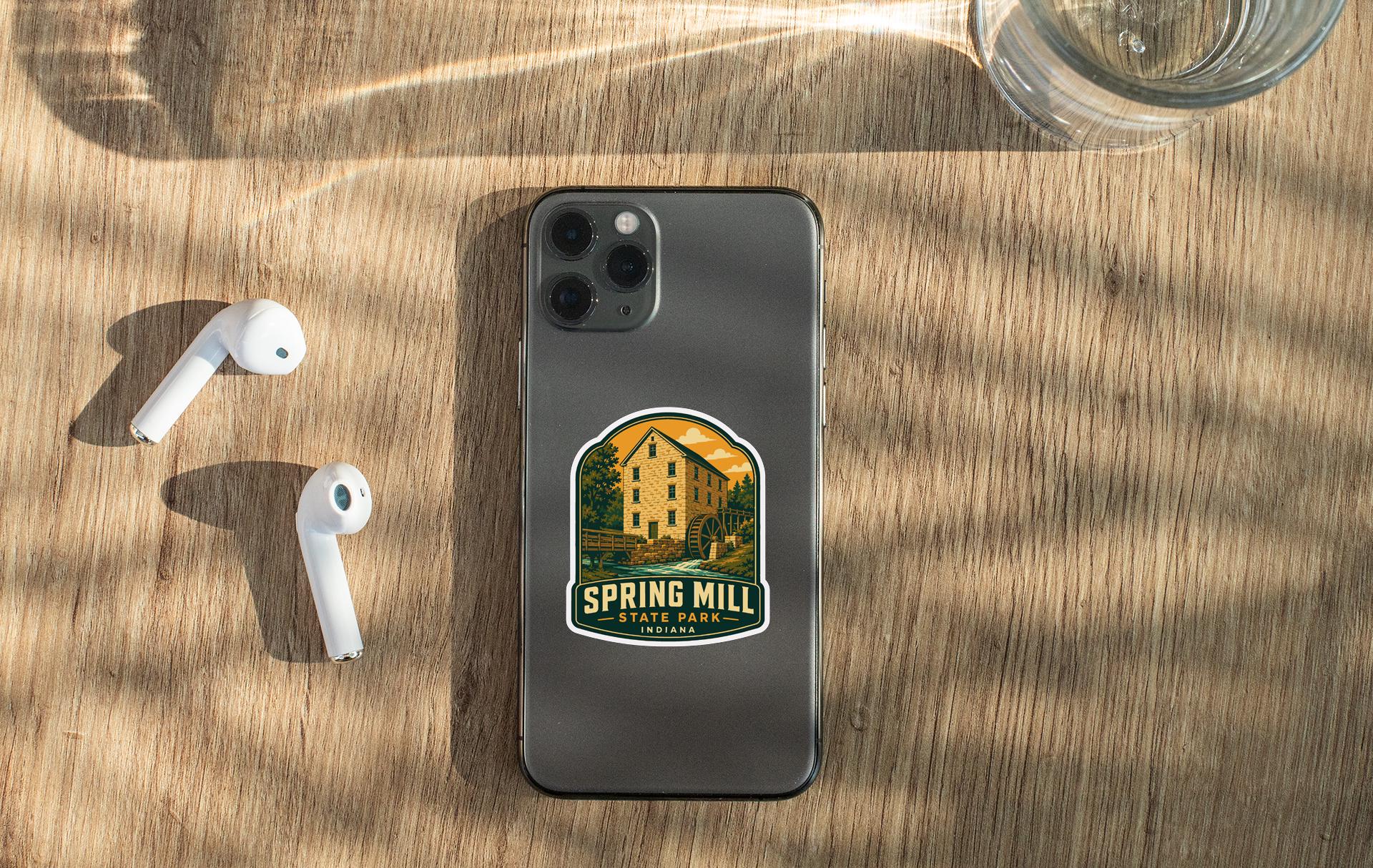 a smartphone with a sticker on it, placed on a wooden surface alongside a pair of white earbuds and a glass of water.