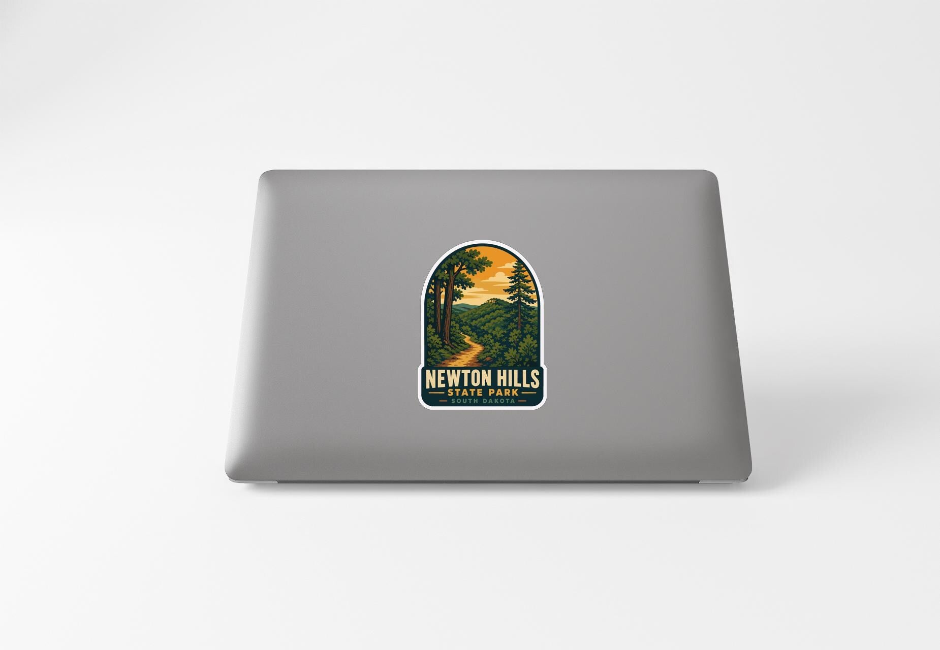 A sticker on the back of a laptop, depicting a scenic landscape with a winding path and trees.