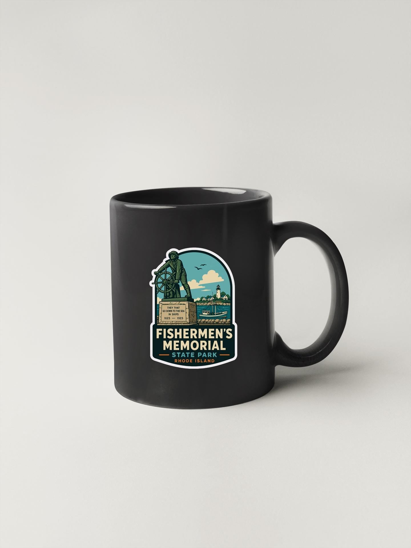 A black coffee mug with a graphic design featuring a statue and the text "FISHERMAN'S MEMORY" and "RHODE ISLAND" printed on it.