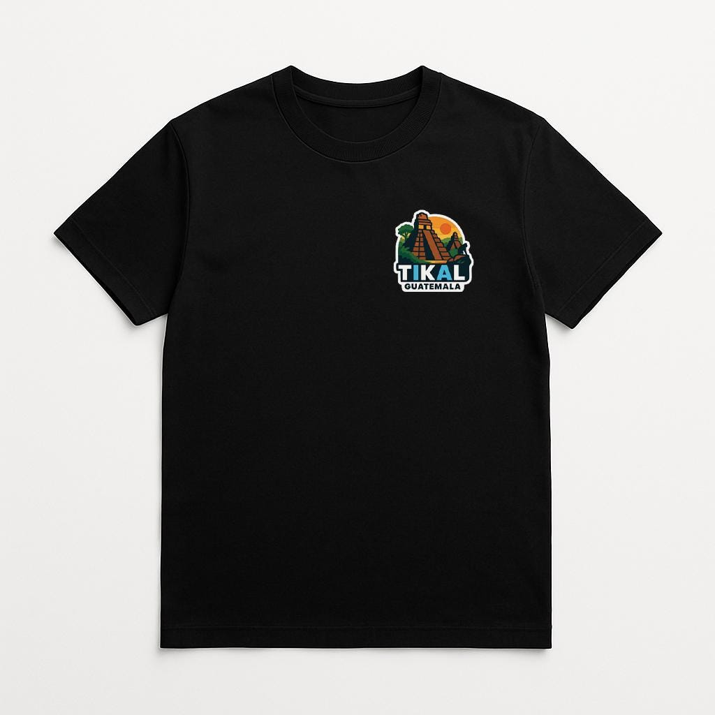 A black t-shirt with a graphic design on the left side, featuring a colorful illustration of a mountain range and the text "TIKAL TEMPLE".