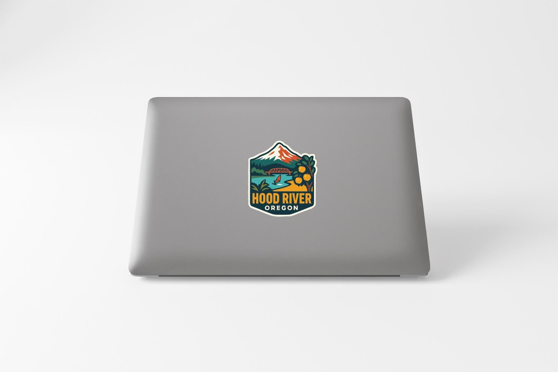 A sticker on the back of a laptop, featuring a mountain landscape with a river and text that says "HOOD RIVER OREGON".