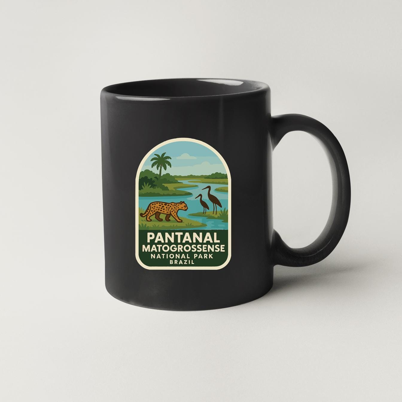 A black coffee mug with a label that features an illustration of a pantan, a bird, and a landscape with a river.