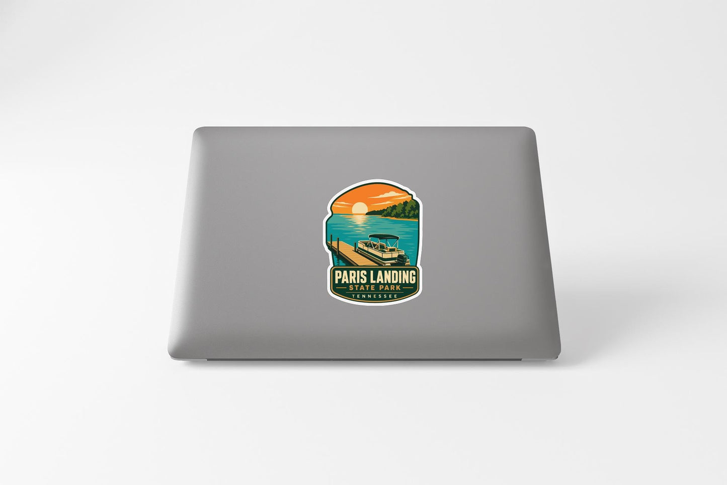 A sticker on the back of a laptop, depicting a scenic view of Paris Landing, with a boat and a sunset in the background.