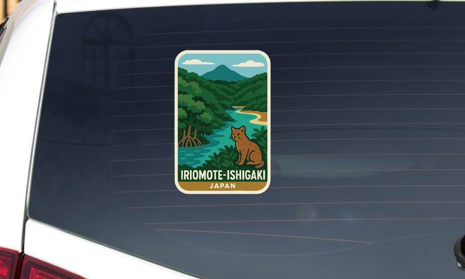 A sticker on the rear window of a car, depicting a scenic landscape with a river, mountains, and a brown cat.